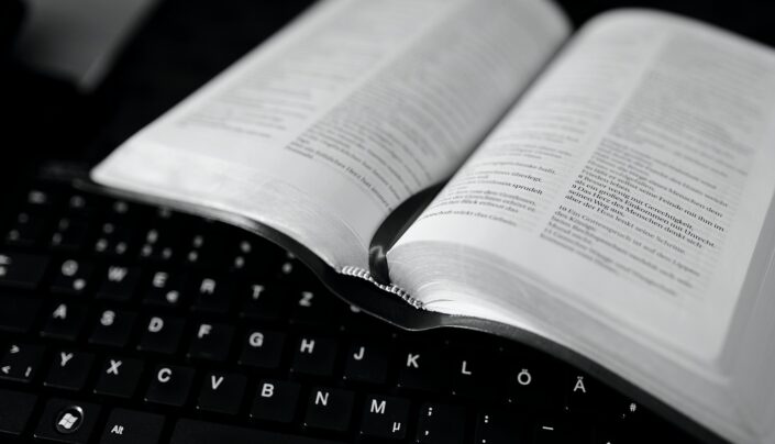 Kuvassa on tietokoneen näppäimistö, jonka päälle on asetettu avattu Raamattu.