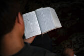 Mies selin kameraan, hänen niskansa takaa näkyy avonainen, persiankielinen Raamattu.