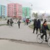 Käveleviä ja pyöräileviä aasialaisia ihmisiä kadulla, taustalla isoja kerrostaloja.