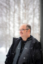 Tom Bollström on kuvattu lumisateessa viistosta. Hänen päällään on tumma takki ja harmaa college. Taustalla näkyy utuisia puita. Bollström katsoo vasemmalle ohi kameran.