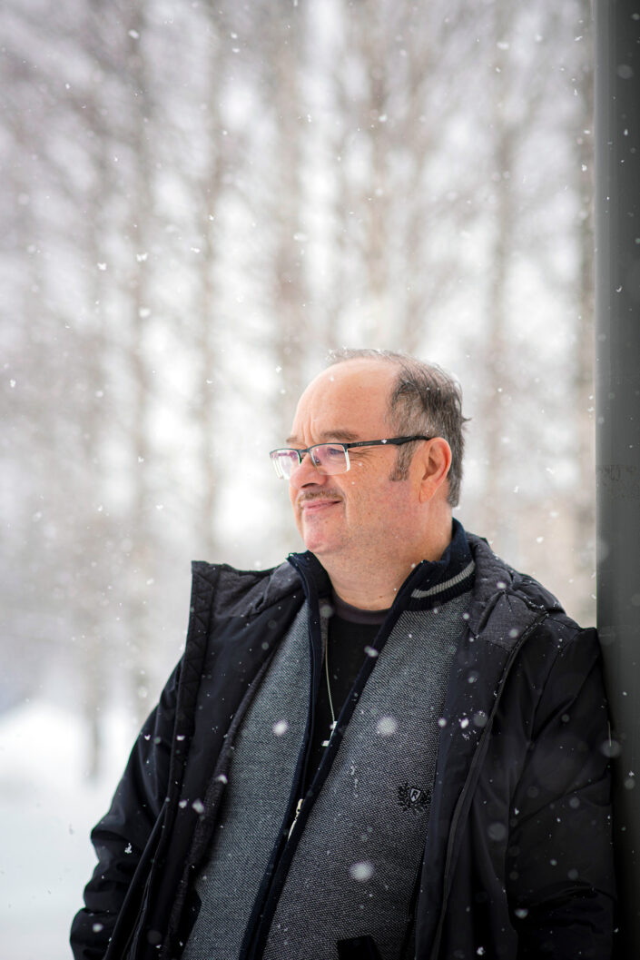 Tom Bollström on kuvattu lumisateessa viistosta. Hänen päällään on tumma takki ja harmaa college. Taustalla näkyy utuisia puita. Bollström katsoo vasemmalle ohi kameran.