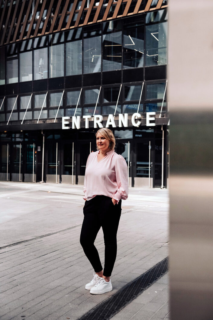Kuvassa on Johanna Vauto, jolla on vaalea polkkatukka, mustat, kapeat housut, valkoiset lenkkarit ja vaaleanpunainen pitkähihainen paita. Hän seisoo Nokia Arenan sisäänkäynnin edessä harmaalla kivetyksellä.
