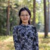 Nainen seisoo mäntymetsässä ja hymyilee kohti kameraa