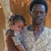 Valokuva afrikkalaisesta miehestä pieni lapsi sylissään.