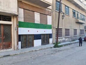 Kadun varrella olevien kerrostalojen seinää syyrialaisessa Homsin kaupungissa. Talon seinään on maalattu suuri Syyrian lippu.