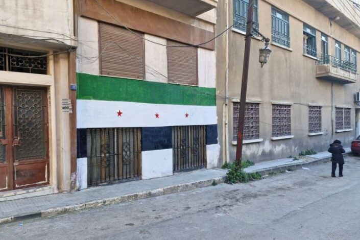 Kadun varrella olevien kerrostalojen seinää syyrialaisessa Homsin kaupungissa. Talon seinään on maalattu suuri Syyrian lippu.