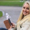 Nainen katsoo kameraan puhelin kädessään ja hymyilee