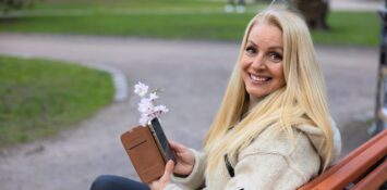 Nainen katsoo kameraan puhelin kädessään ja hymyilee