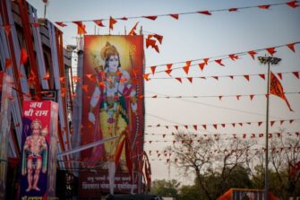 Intialainen katu, jonka ylle on ripustettu oransseja viirilippuja; rakennusten seinissä suuret hindujumalia kuvaavat julisteet.