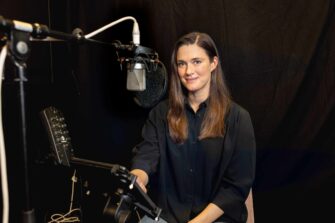 Tummahiuksinen nainen katsoo studiossa kameraan ja hymyilee