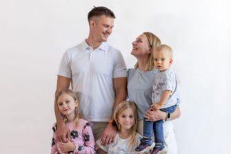 Perhe, jossa kaksi aikuista ja kolme lasta hymyilevät