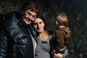 ukrainalainen nuori äiti lapsi sylissä. suomalainen nainen vieressä. hymyilevät.