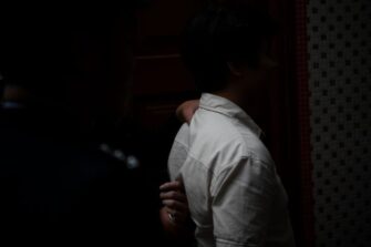 Kädet tarttuvat miehen niskaan ja selkään takaapäin, kummankin ihmisen kasvot jäävät pimeään.