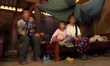 Mies istumassa tuolilla poika sylissään ja nainen ja tyttö istumassa vierekkäin sängyllä. Ihmisten kasvot on sumennettu.