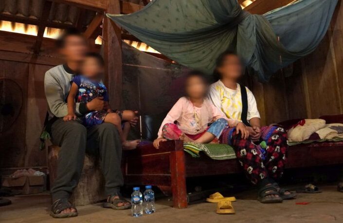 Mies istumassa tuolilla poika sylissään ja nainen ja tyttö istumassa vierekkäin sängyllä. Ihmisten kasvot on sumennettu.