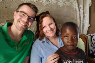 Kaksi aikuista ja lapsi hymyilevät kameralle.