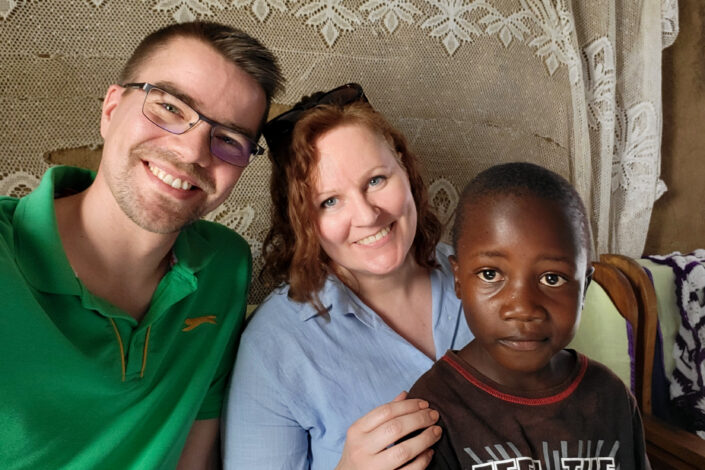 Kaksi aikuista ja lapsi hymyilevät kameralle.