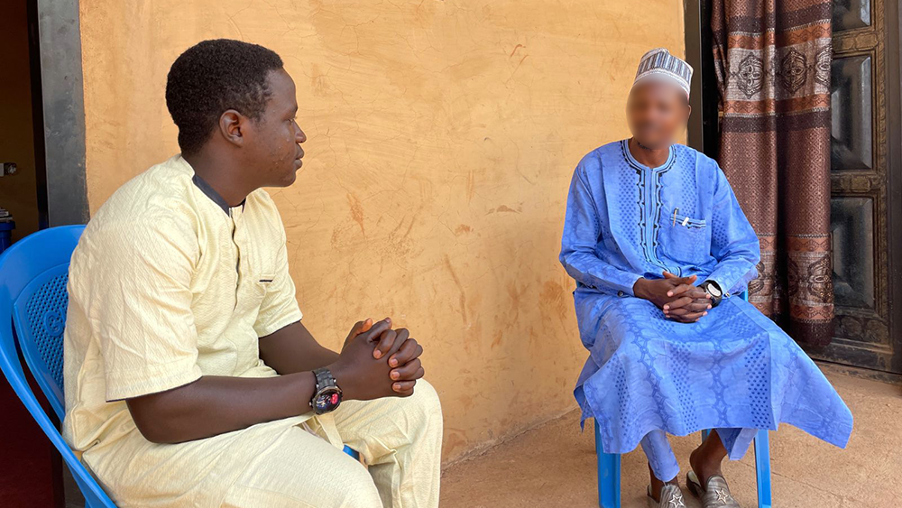 Kaksi nigerialaista miestä istumassa tuoleilla kädet ristissä puhumassa keskenään. 