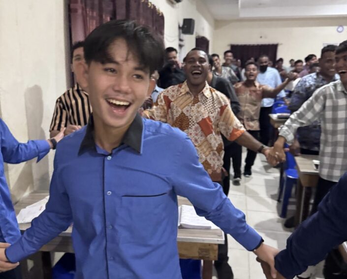 Kymmeniä iloisia oppilaita käsi kädessä laulamassa ja ylistämässä. 