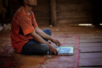 Mies istuu lattialla edessään kasa koulukirjoja ja vihkoja.