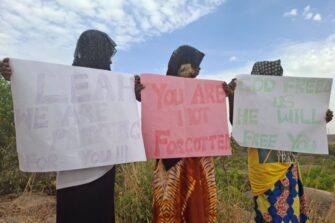 Kolme afrikkalaista nuorta naista käsissään suuret julisteet, joihin on kirjoitettu englanniksi tekstejä, joissa luvataan rukoilla Leah Sharibun puolesta.