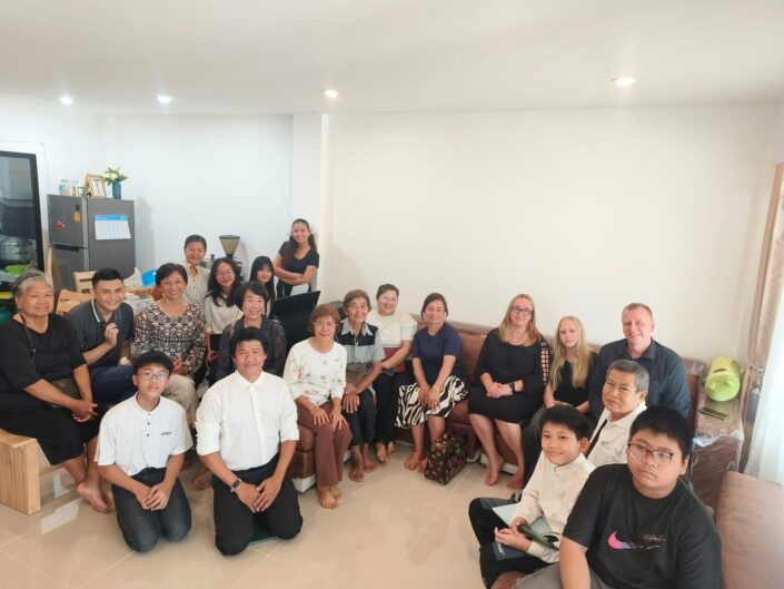 Joukko ihmisiä istuu olohuoneessa ja hymyilee