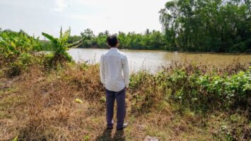 Mies seisoo joen rannalla selin kameraan.