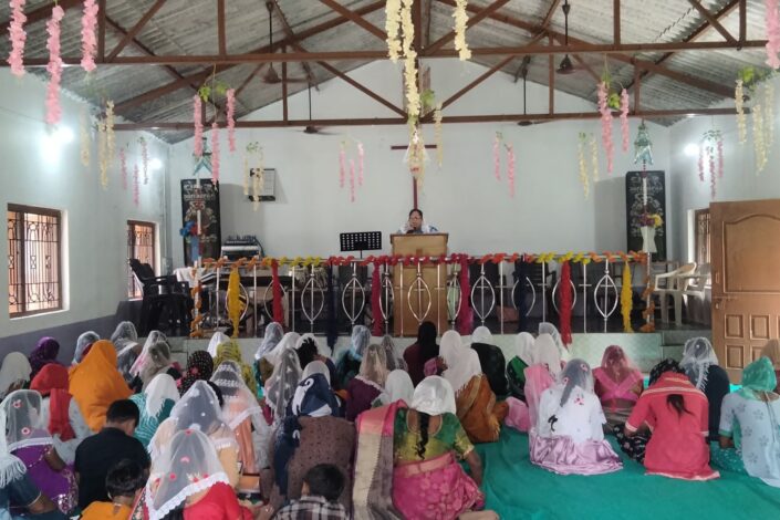 Intialaisia naisia kirkkosalissa, takaapäin kuvattuna.