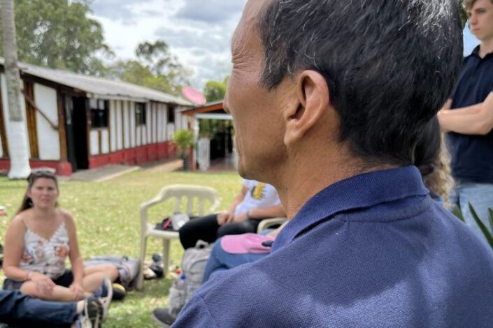 Mies kuvattuna takaviistosta. Hänen edessään istuu nuoria.