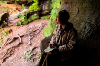 Aasialainen nainen istuu suuren puun juurella Raamattu sylissään.