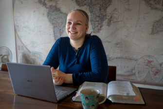 Susanna Sorila, vaaleahiuksinen nainen sinisessä paidassa, istuu pöydän äärellä edessään avoin Raamattu ja tietokone.