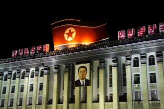 Suuri rakennus, jonka katolla on valtava Pohjois-Korean lippu ja etuseinällä roikkuu iso Kim Il Sungin muotokuva.
