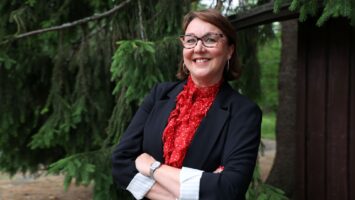Lea Pääkkönen hymyilee suuren kuusen juurella.