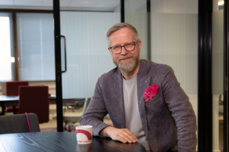 Mies toimistossa katsoo suoraan kameraan ja hymyilee