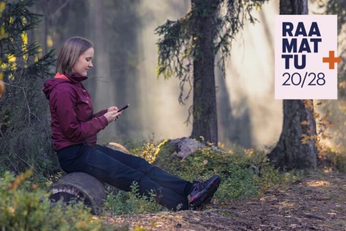 Nainen metsässä lukee puhelimella Raamattua